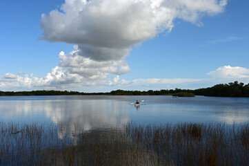 Distant kayakers on calm water of Nine Mile Pond in Everglades National Park, Florida on sunny afternoon under striking winter cloudscape.