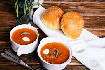 Thick tomato soup with meat in white tureens. Homemade buns, sauce, sage.