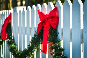Christmas holiday outdoor decorations with red ribbon bows and green pine garland on white picket...