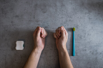  Woman hand holding a dental floss on the dark, concrete background. Dental care.