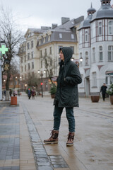 a guy in a jacket with a hood stands in the middle of the city