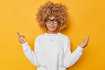 Portrait of beautiful woman with curly hair practices yoga indoors holds hands in mudra gesture...