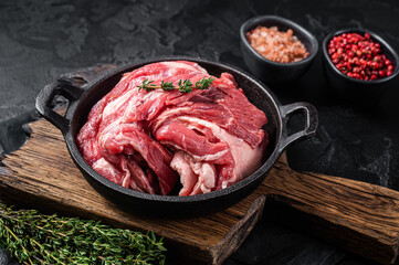 Boneless lamb neck, raw meat in a skillet with herbs. Black background. Top view