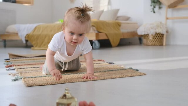 The first year of a baby's life. Cute baby learns to crawl on his knees in the house. Curious baby crawls on the floor in the house.