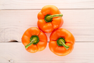 Three orange fresh sweet peppers on a wooden table, close-up, top view.