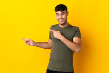 Young Colombian man isolated on yellow background surprised and pointing side