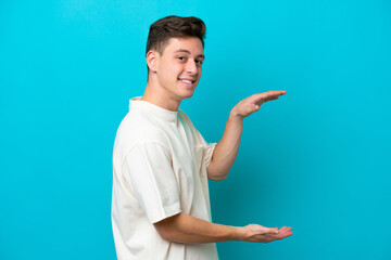 Young handsome Brazilian man isolated on blue background holding copyspace to insert an ad