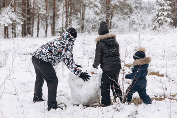 Happy father and sons rolling big snowball together for snowman in snowy winter forest. Man Joyful...