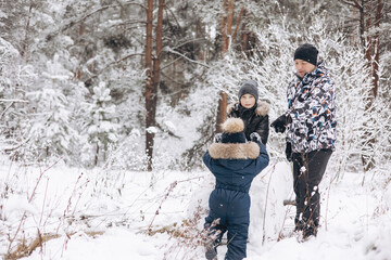 Fototapeta na wymiar Happy father and sons rolling big snowball together for snowman in snowy winter forest. Man Joyful teenager and little boy playing and having fun on family walking. Wintertime activity outdoors.