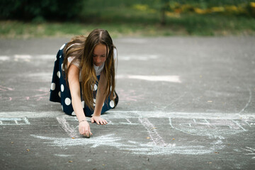 A girl draws with chalk on the pavement.