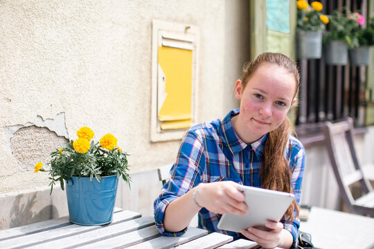 A teengirl sits with a her tablet in an outdoor city cafe