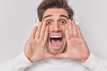 Headshot of emotional young man screams loudly keeps hands near mouth stares impressed at camera...