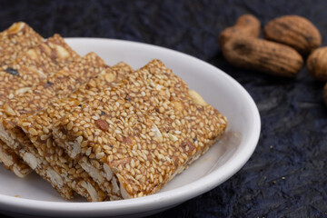 Indian sweet Mithai for Makar Sankranti Lohri Gajak Also Known As Gur Gajjak Gazak Gachak Til Patti Papdi Chikki Made Of til sesame seed Jaggery Gud Almond Badam Pistachio  deep blue background