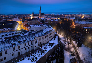 The historic, Moravian city of Olomouc. Evening, aerial view of the historic center, covered with snow. Blue hour, glowing lamps, blue and orange. Regional center of Moravia. - obrazy, fototapety, plakaty