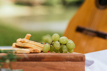 Uvas en una tabla de madera con palillos de pan y una guitarra al fondo