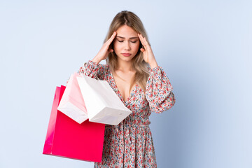 Teenager Russian girl with shopping bag isolated on blue background with headache