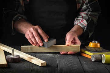 Woodworker cleans a wooden plank with an abrasive tool. Hands of the builder close-up during work. Renovation or construction idea
