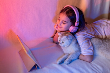 A happy little girl in pink headphones, with a white adorable cat in neon light
