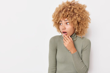 Fototapeta na wymiar Scared shocked blonde woman holds breath keeps mouth opened stares bugged eyes wears casual turtleneck isolated over white background with copy space for your advertising content. Human reactions