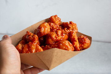 A view of a hand holding a tray of glazed boneless chicken wings.