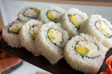 A closeup view of a hand holding a  plate of California rolls.