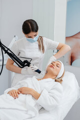 Obraz premium A young girl gets a carbon peeling for the skin of the neck in a beauty salon. Laser pulses cleanse the skin. Hardware cosmetology. The process of photothermolysis, warming the skin.