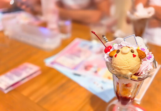 Japanese milk tea ice cream and almonds shaped as a cute bear character topped with sweet whipped cream and cherries in a glassware full of corn flakes against a blurry background.