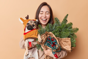 Positive Asian woman laughs out hears something very funny poses with favorite pet and New Year...