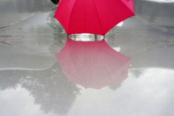 Roter aufgespannter Regenschirm auf Wasserrutsche mit Spiegelung im Schwimmbad bei Regen im Sommer