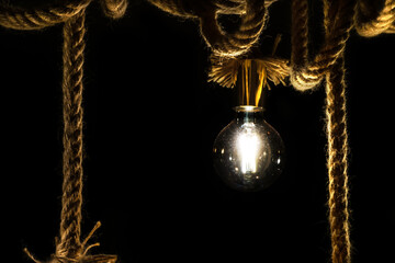 old light bulb on rope in front of black background  