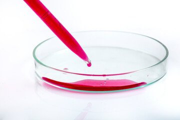 Laboratory pipette with drop of red liquid over Petri dishes with red biological analysis solution...