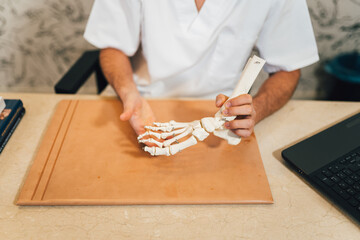 Chiropodist male doctor with white medical gown explaining diagnosis to a patient with an articulated bone foot model