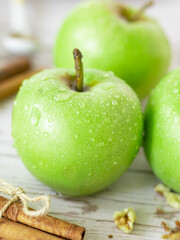 Fresh green Granny Smith apples with water drops on a wooden table with cinnamon sticks. A closeup. 