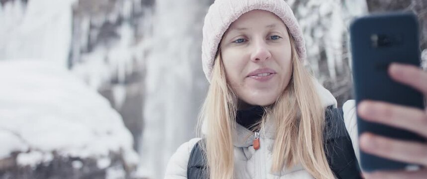 Woman takes selfie photo hiking at winter Alps waterfall in close up