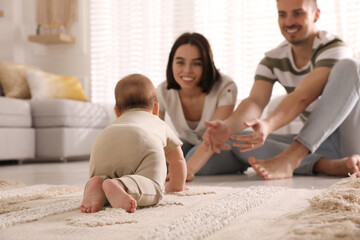 Happy parents watching their cute baby crawl on floor at home - obrazy, fototapety, plakaty