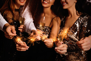 Friends with glasses of sparkling wine and sparklers celebrating New Year, closeup
