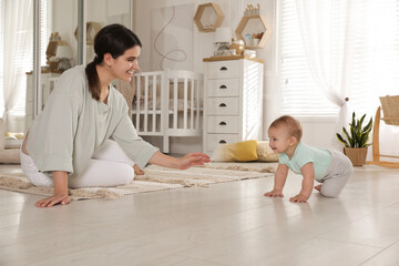 Happy young mother watching her cute baby crawl on floor at home