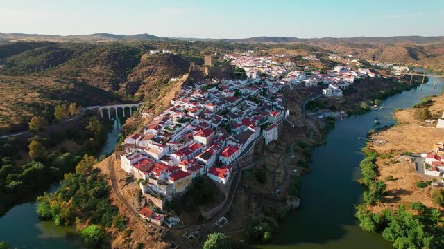 Beautiful Portuguese landscape village with a medieval castle and bridge in 4K. Drone footage from above of Castle of Mertola surrounded by many traditional colored houses by a river in Beja, Portugal