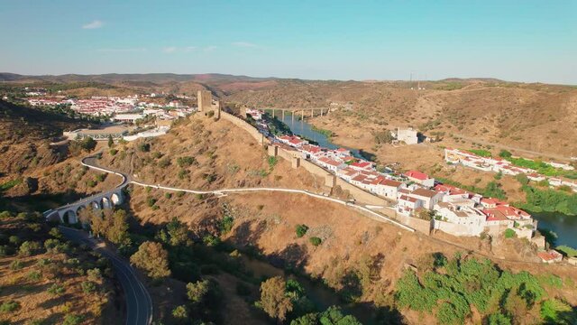 Beautiful Portuguese landscape village with a medieval castle and bridge in 4K. Drone footage from above of Castle of Mertola surrounded by many traditional colored houses by a river in Beja, Portugal