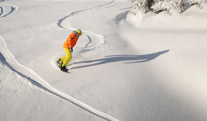Snowboarder in orange jacket and yellow pants drives down the piste. Winter sport and recreation,...