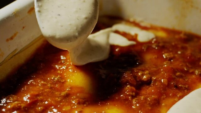 Pouring white bechamel sauce over lasagne in slow motion, italian food close up