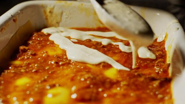 Pouring bechamel cream sauce ingredient during the preparation of lasagne meal