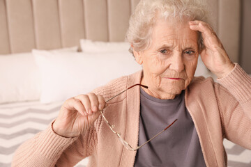 Senior woman with headache in bedroom at home - obrazy, fototapety, plakaty