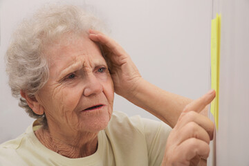 Senior woman looking at reminder note indoors. Age-related memory impairment