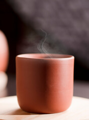 Earthenware mug with hot steam, with tea on white wood, dark background.