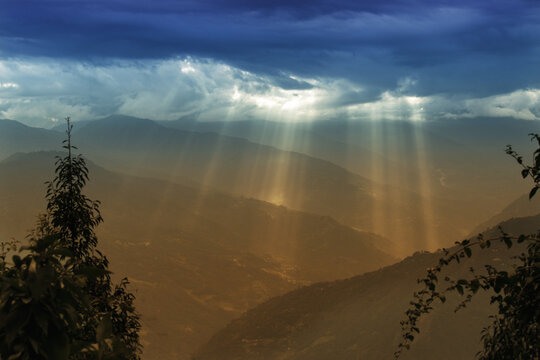 Sun rays coming out of cloud burst - at Rabangla, Sikkim, India. Trees in foreground and Himalayan mountains in background.