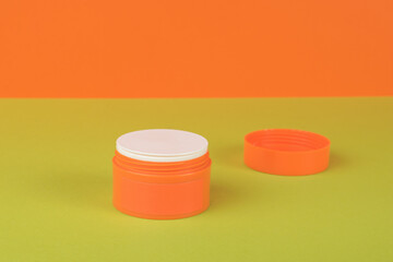 An open orange jar with cream on a green and orange background.
