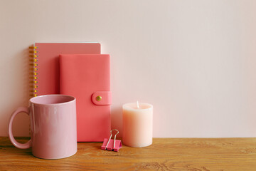 Pink notebook, mug cup, candle on wooden desk. workspace
