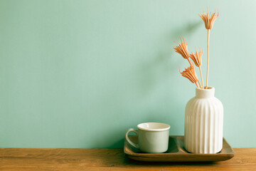 Mug cup with vase of dry flowers on wooden table. mint wall background