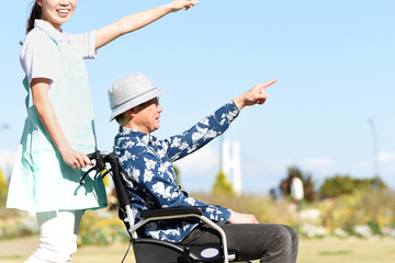 青空の屋外で車椅子を押す若い介護士の女性とシニア男性